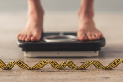 woman standing on a scale with a tape measure sitting in front