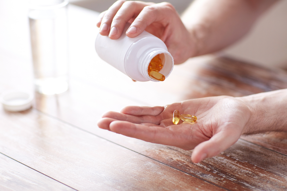 man pouring fish oil supplement into hand from a medicine bottle