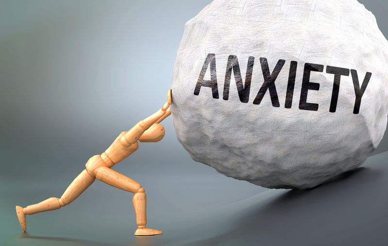 wooden human figure pushing boulder labeled anxiety up a hill