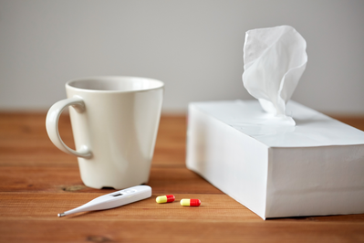 tissue box, coffee cup, thermometer, and medication sitting on a wooden table
