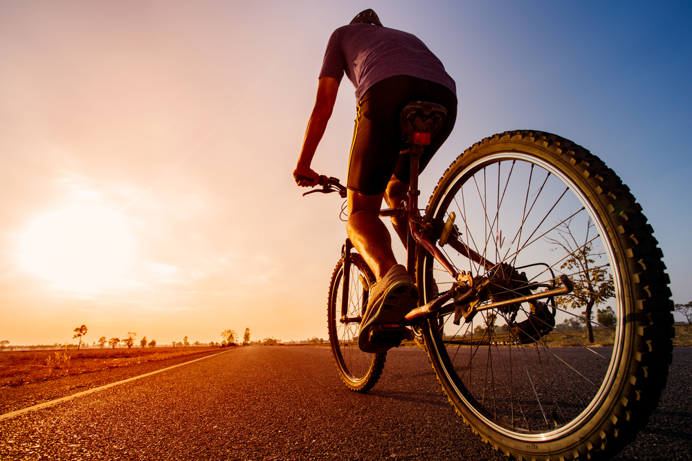 a man riding his bicycle on a road at sunset