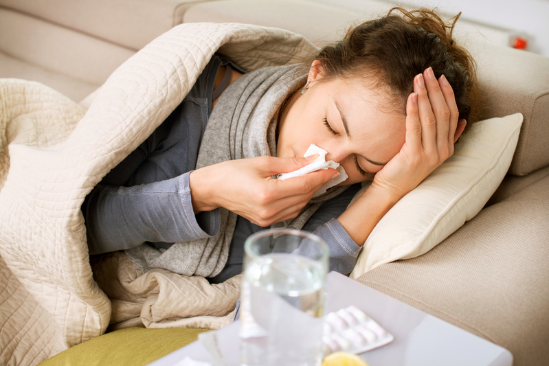 woman sick with flu lying on couch sneezing into tissue
