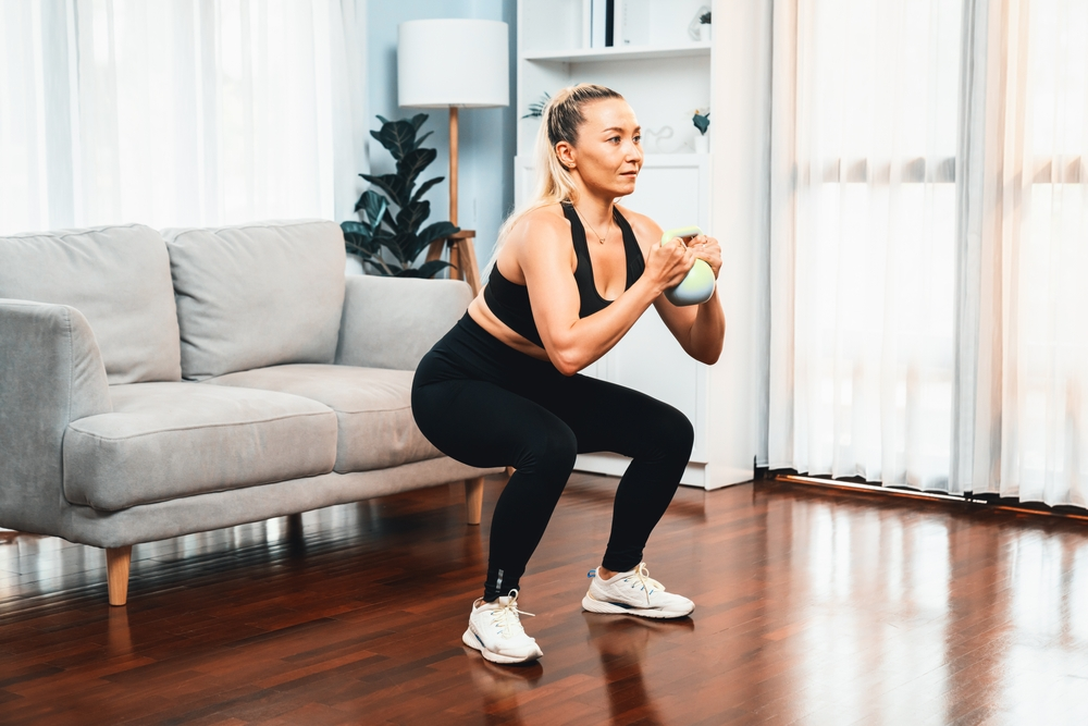 woman doing squats while holding dumbbell in living room