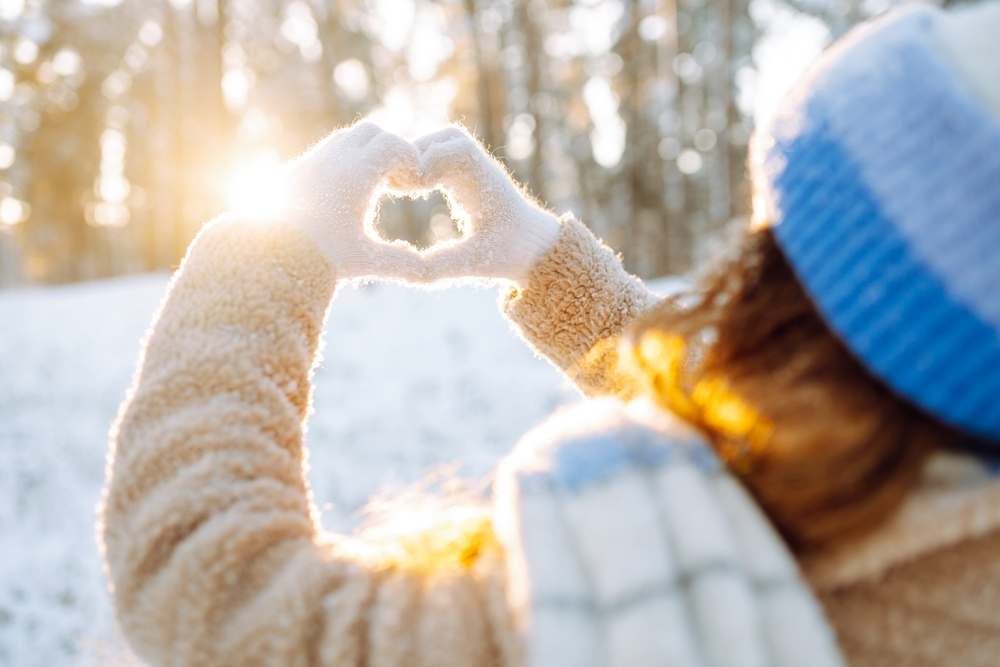 woman enjoying a sunny winter day making a heart shape with her hands