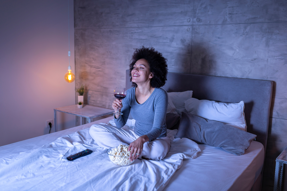 woman eating, drinking, and watching TV in bed at night