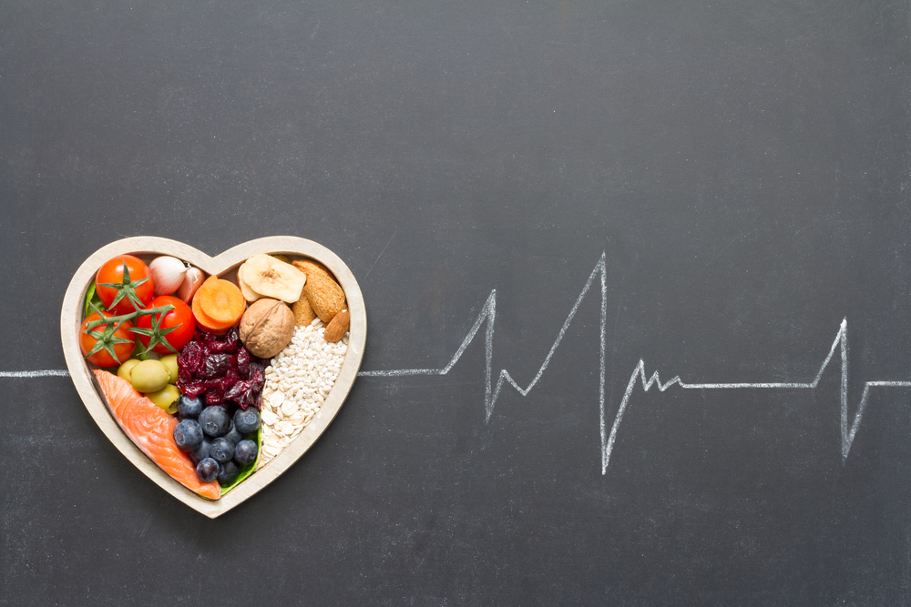 heart-healthy foods in heart shaped bowl on blackboard with chalk cardiograph