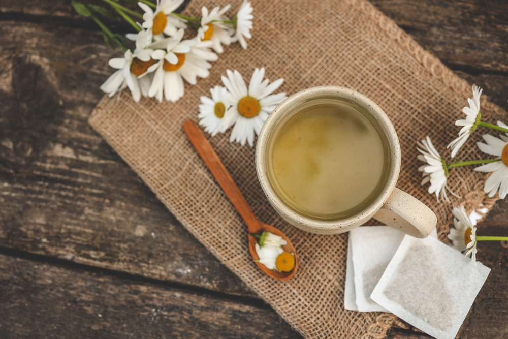 chamomile tea bags and cup of tea surrounded by chamomile flowers